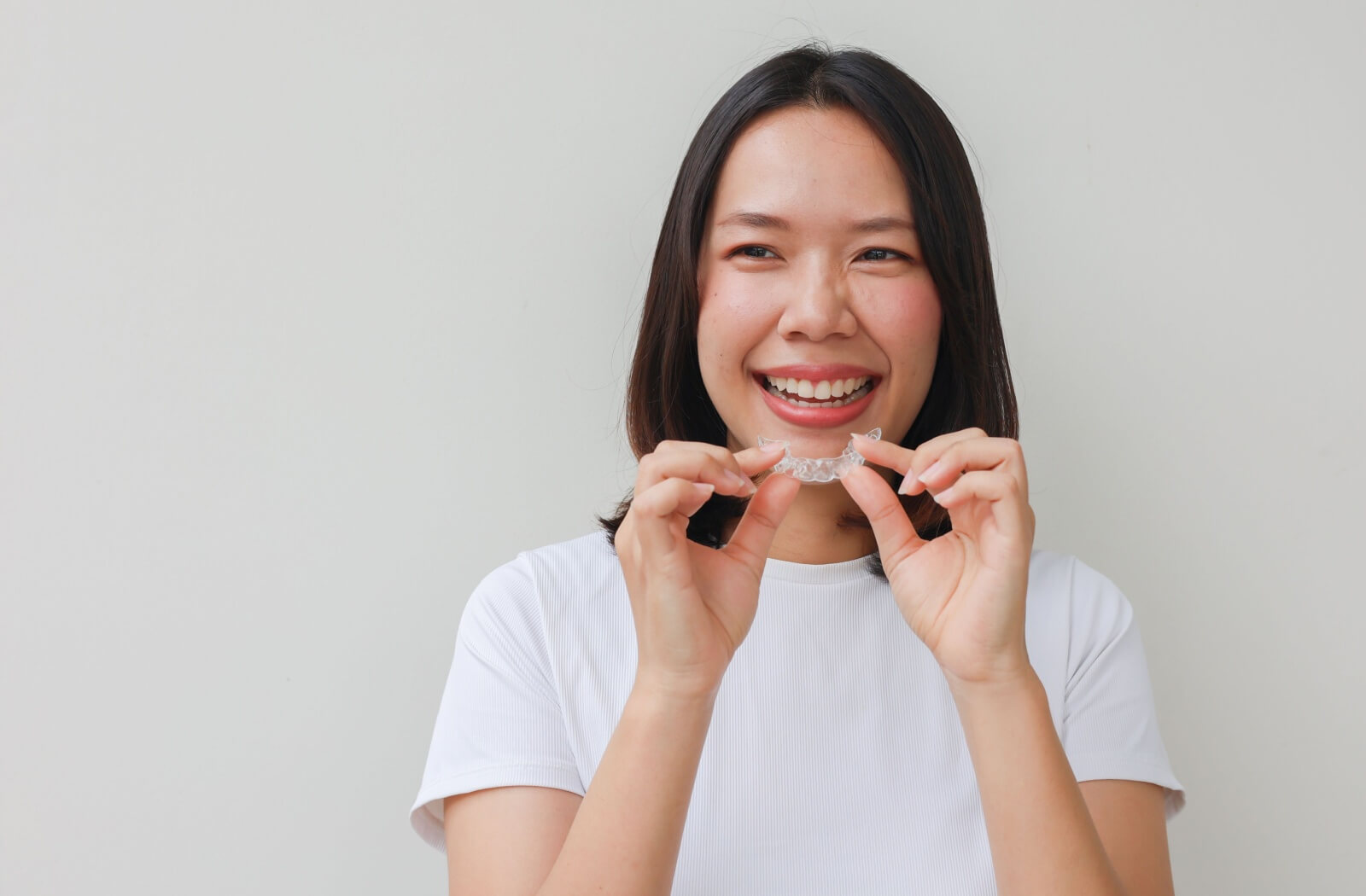 A smiling adult puts their clear aligners back in after chewing gum.