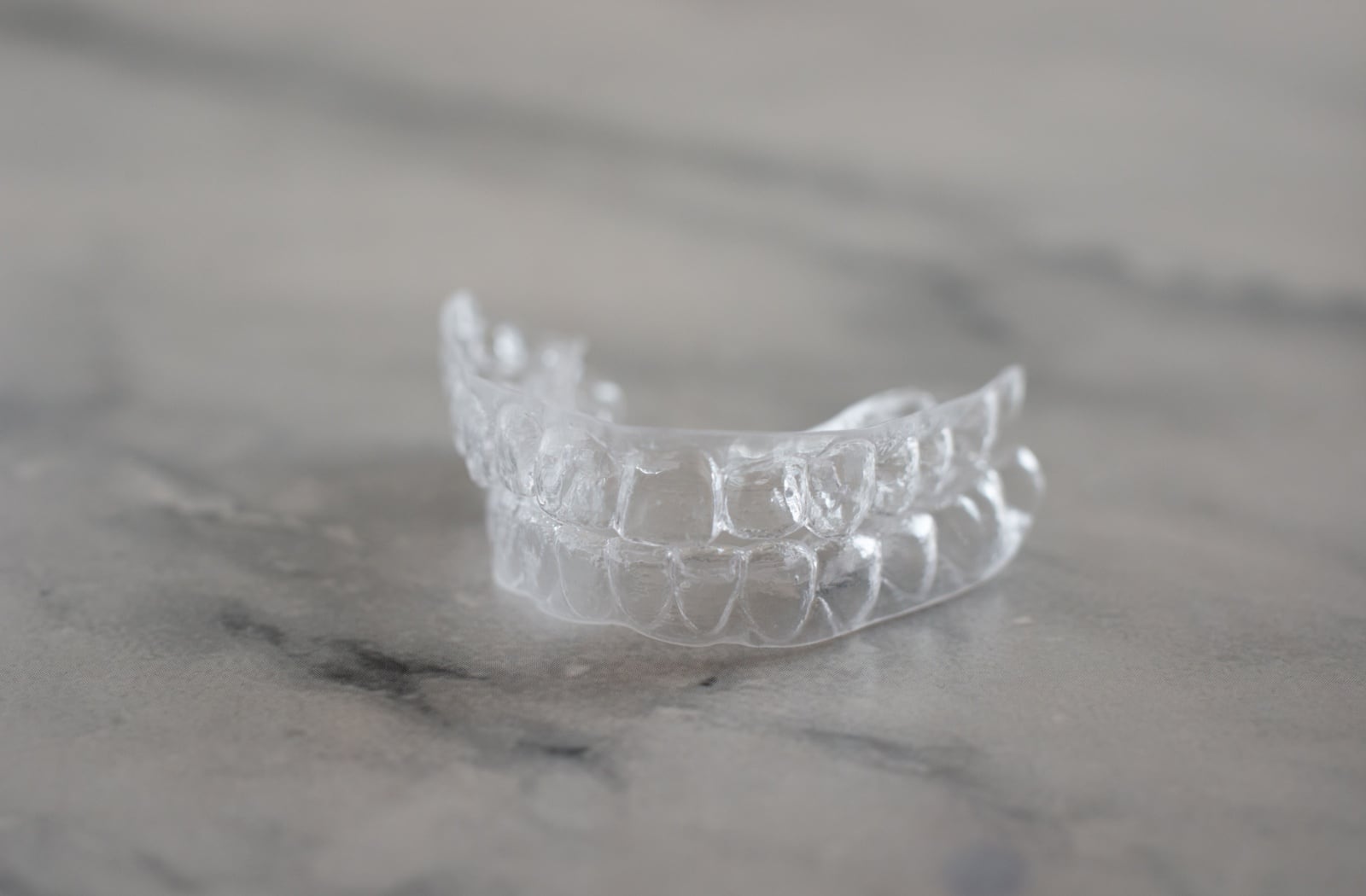 Smiling person holding a clear aligner near her teeth, preparing to insert it for orthodontic treatment.