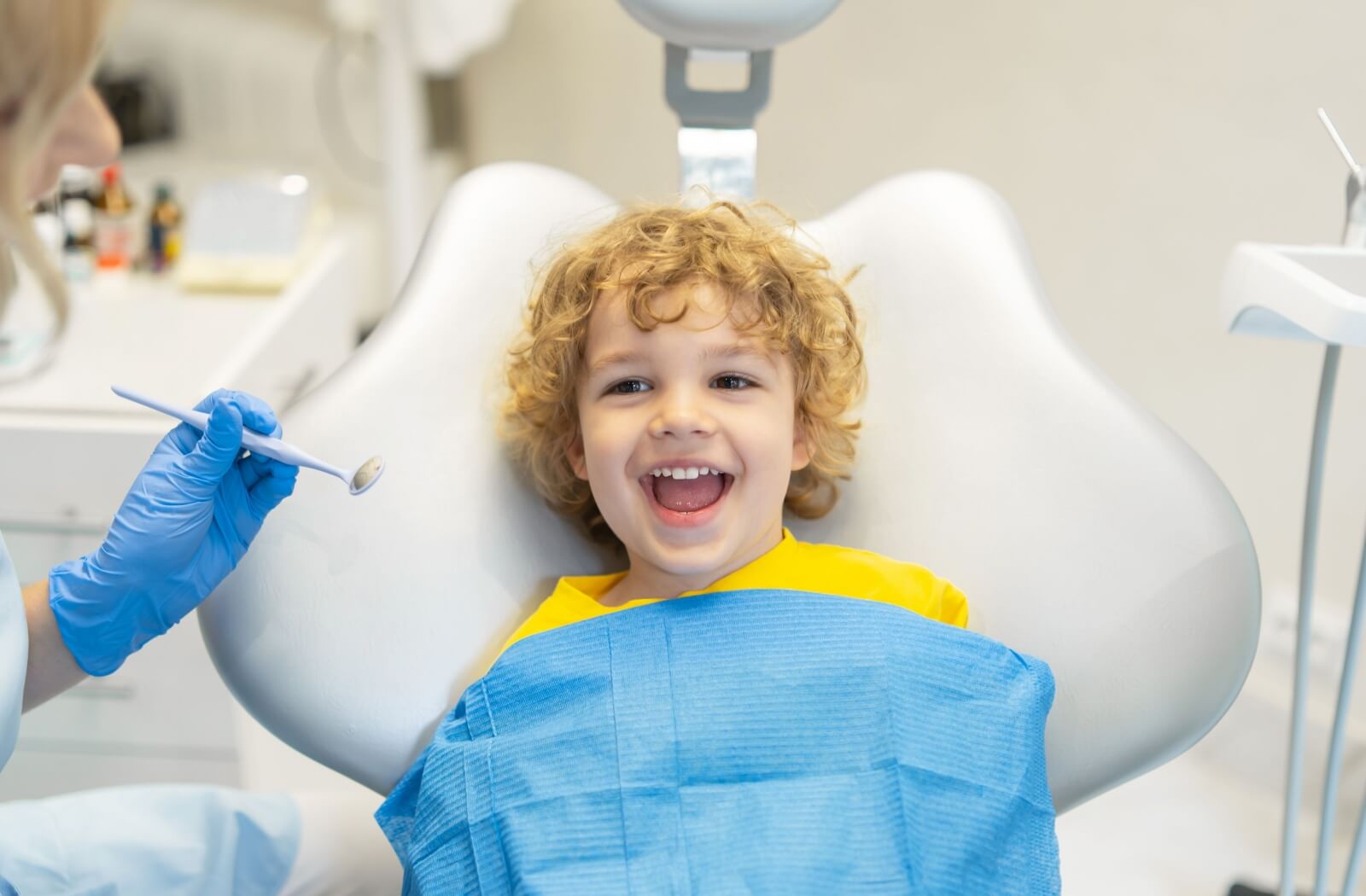 A child smiles as they sit in the dentist chair, about to get their teeth examined.