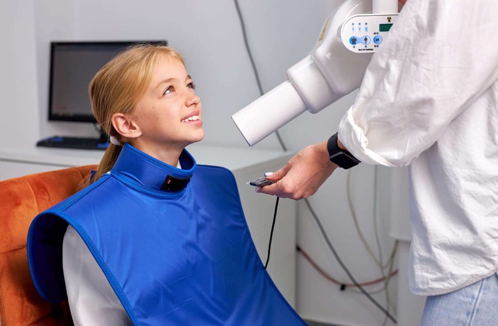 A child prepares for a dental X-ray, wearing a special protective apron.