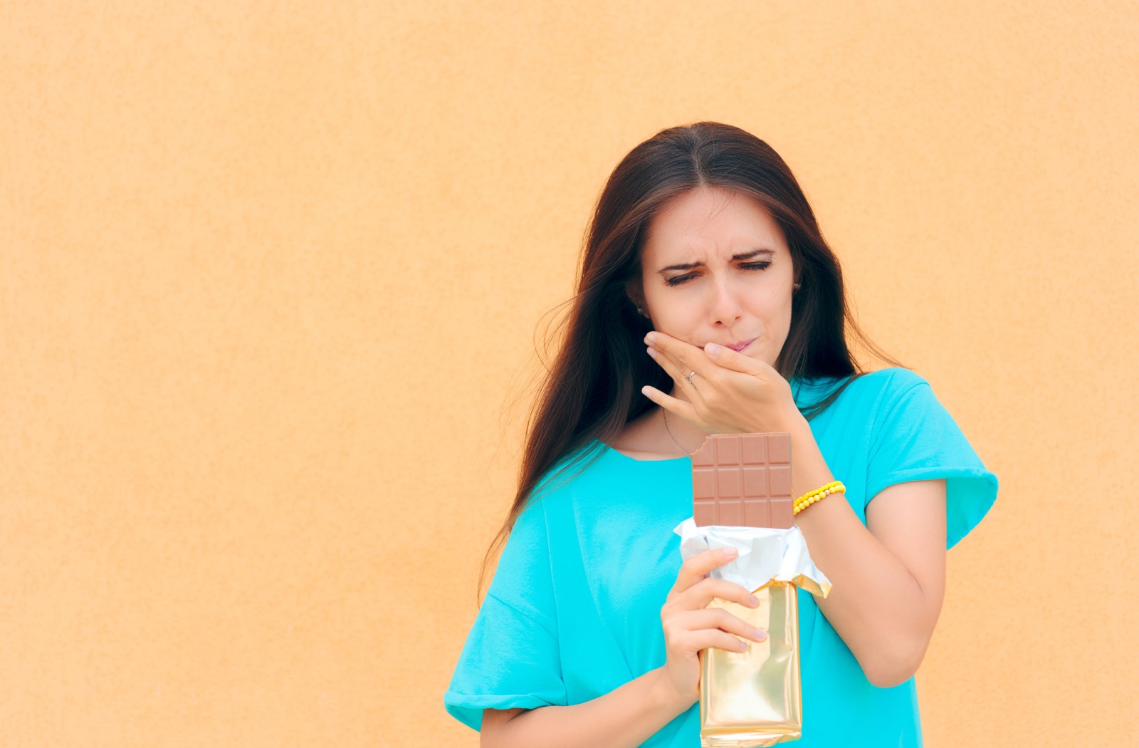 A frowning adult experiences a toothache after biting into a chocolate bar.