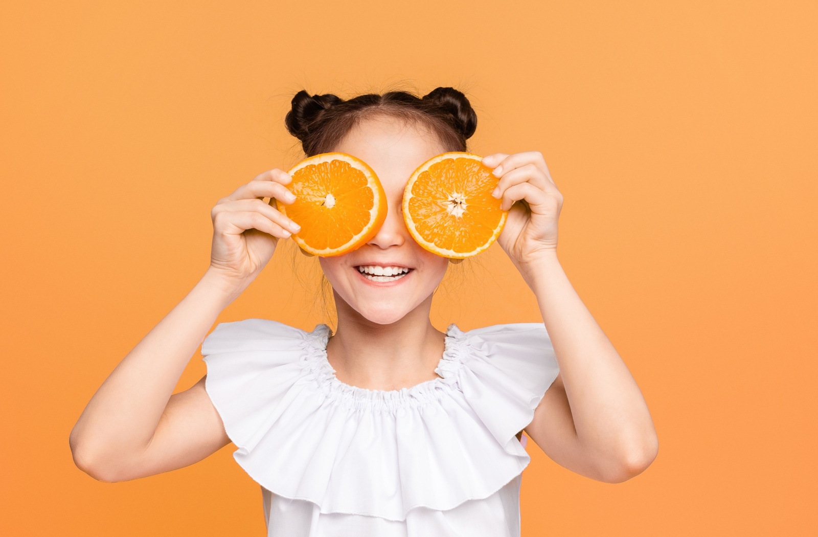 A young child holding two circular slices of orange fruit up to her eyes.